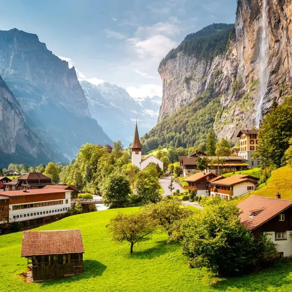 A picturesque swiss village nestled in a valley with lush green fields and towering mountain cliffs.