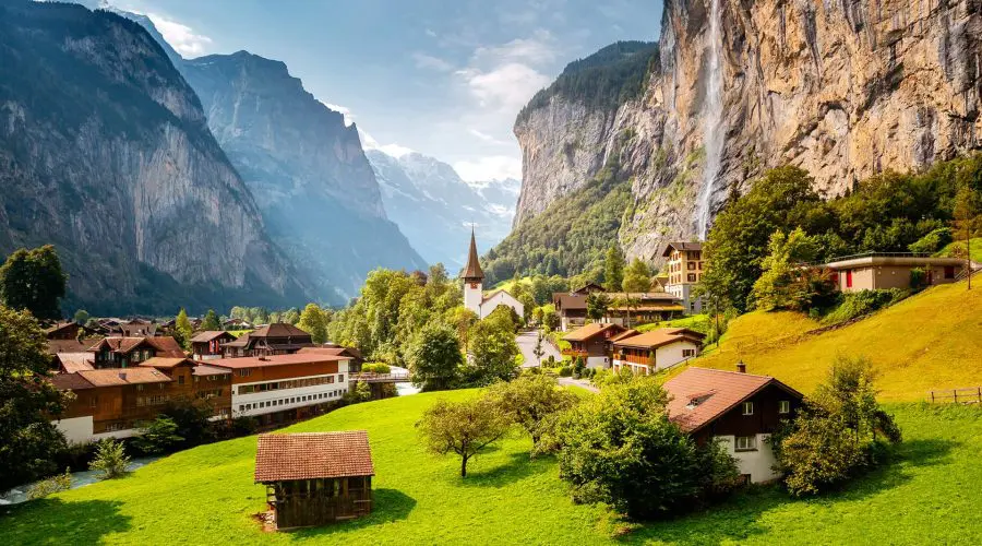 A picturesque swiss village nestled in a valley with lush green fields and towering mountain cliffs.