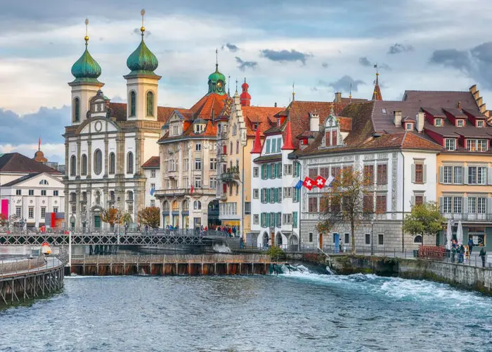 Picturesque view of lucerne, switzerland, featuring historic buildings, a church with twin towers, and a bridge over a flowing river.